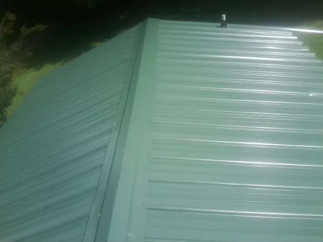 New green metal panels meeting at the ridge of a roof — Flat Roof Repair work by our crew in Augusta